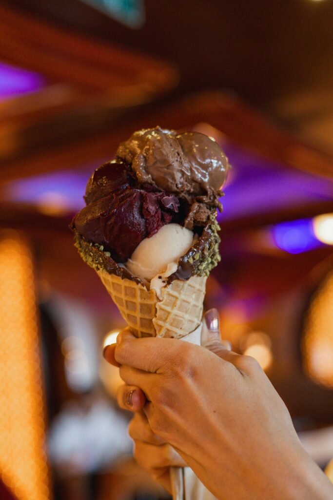 Close-up of a hand holding a multi-scoop ice cream cone with varied flavors and colors.