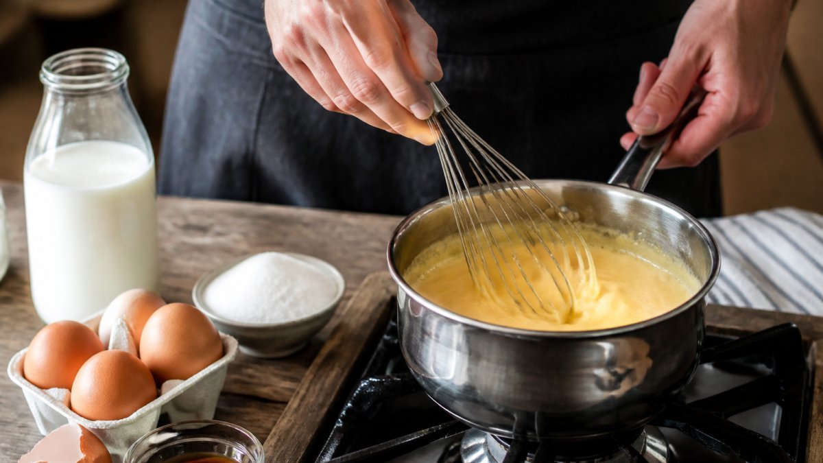 Hands whisking ingredients in a saucepan to make homemade custard vs grocery store quality dessert.